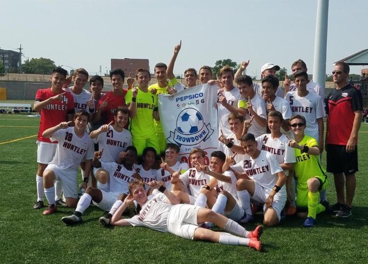 Huntley boys soccer posing with their banner after winning the championship of the PepsiCo Showdown (Courtesy of Huntley_Soccer Twitter).