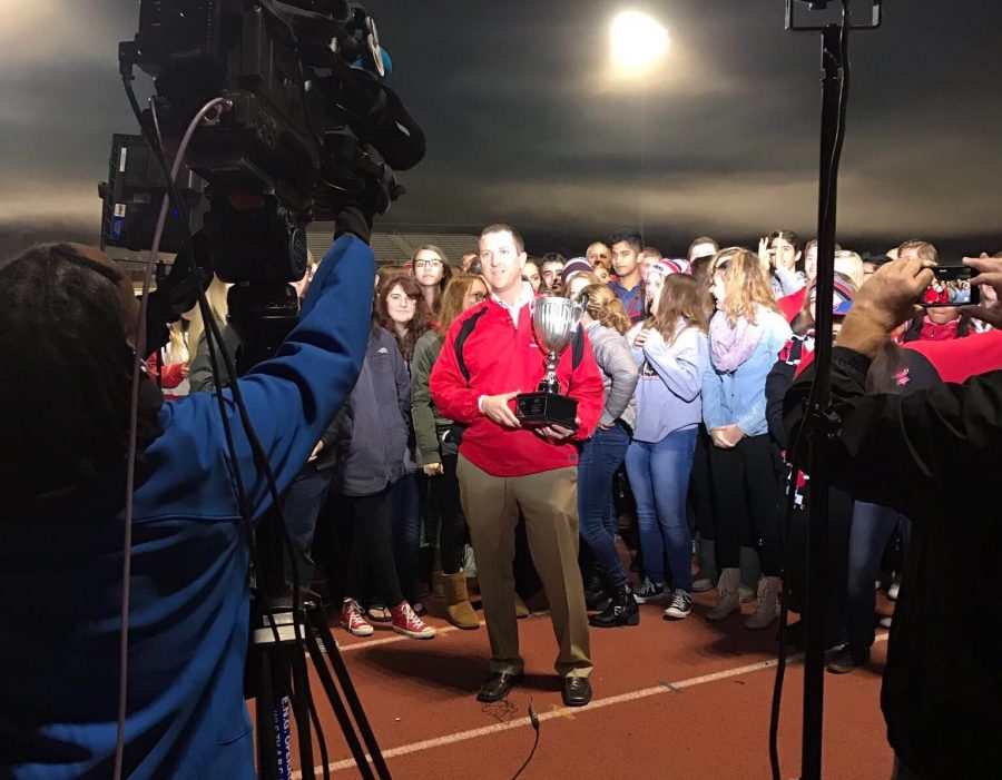 Principal Scott Rowe holds the trophy while live on ABC 7 Chicago (Courtesy of HHS Athletics twitter)