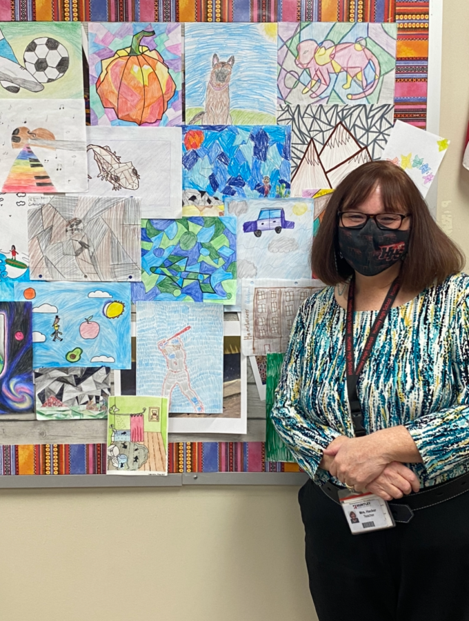 Valerie Hacker stands proudly next to her colorful board of student artwork.