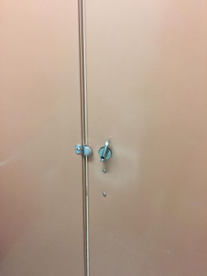 Bathroom stall door being held closed shut with a foot propped up while ignoring the cracks between the door.