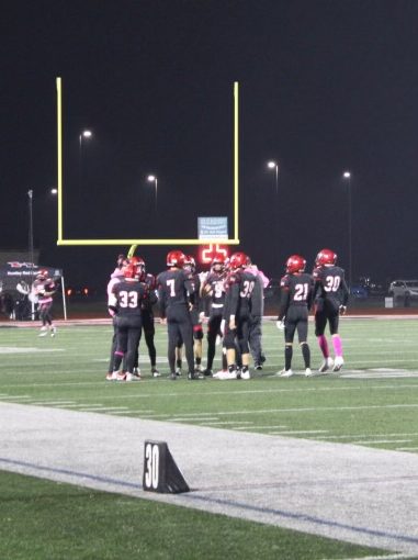 A group of football players stand on the field, discussing their next play.