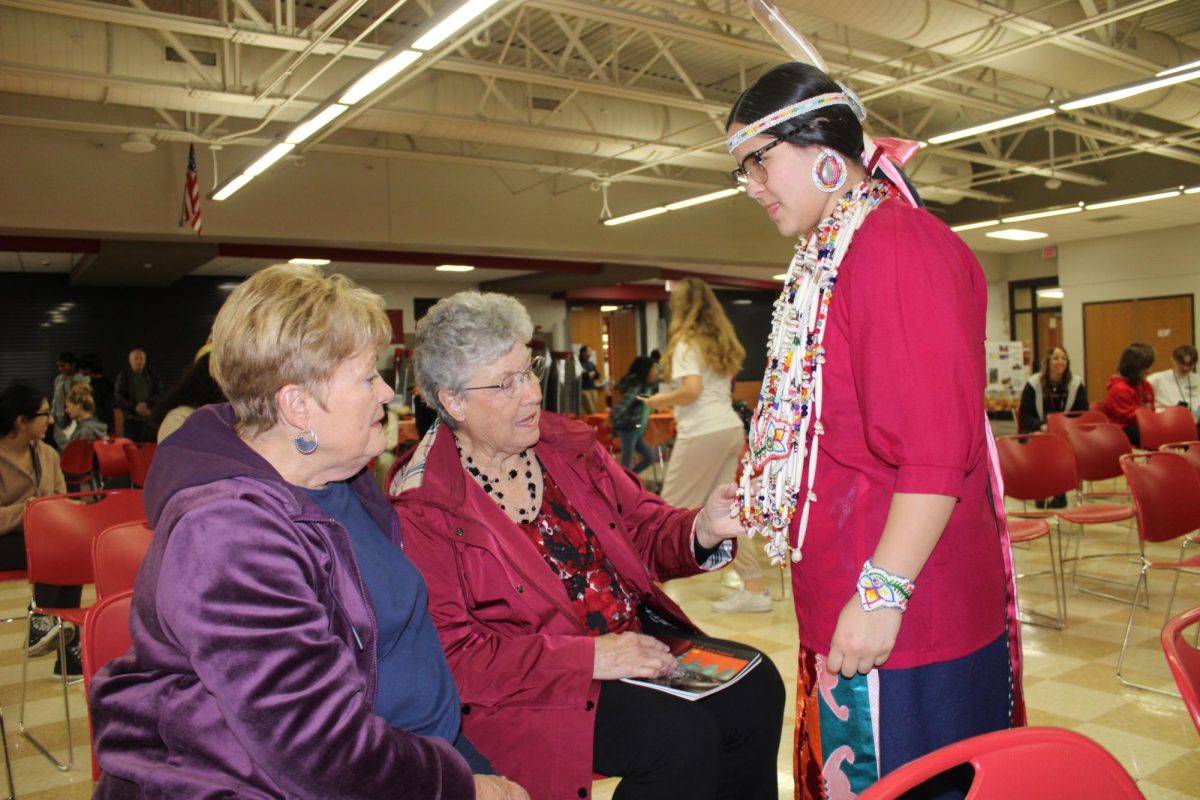 Older adults admiring an Indigenous persons beaded necklace.