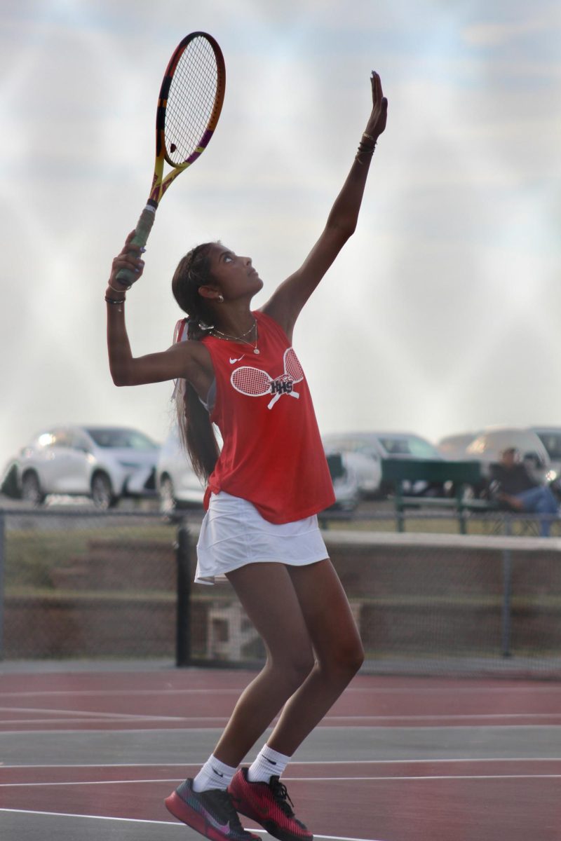 Senior Vinuthna Depala tosses the tennis ball high into the air, preparing to serve it.