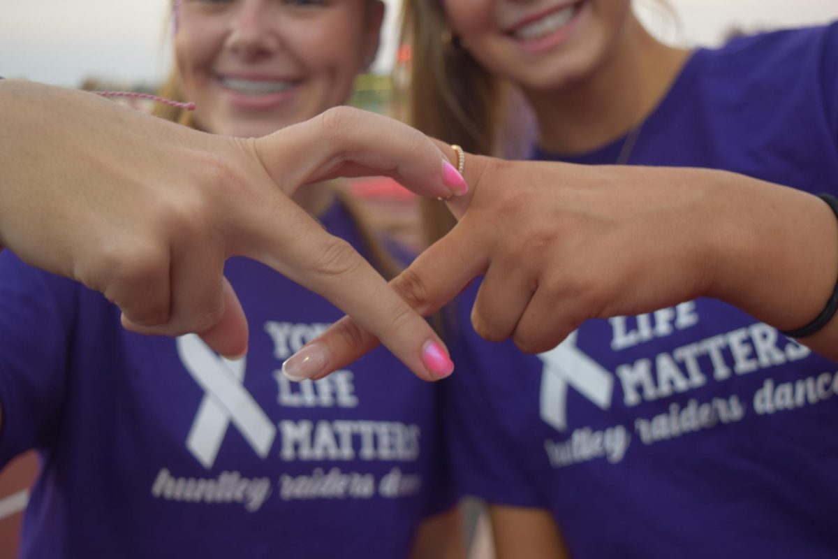 Juniors Addy Zay and Ashlyn Murphy making an awareness ribbon with their hands.