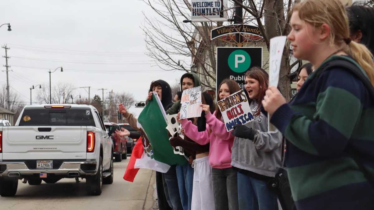 Students wave a Mexican flag and hold protest signs along Harmony Road in Huntley on Feb. 20 as part of a walkout opposing U.S. Immigration and Customs Enforcement operations.
